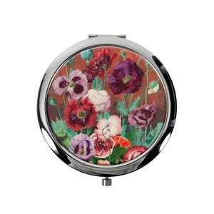 Può includere: Un specchietto compatto rotondo argentato con una pittura floreale. L'opera d'arte presenta un bouquet di fiori colorati, tra cui papaveri rossi, viola e bianchi, su uno sfondo rosso-marrone. Lo specchietto compatto ha un'apertura a cerniera.