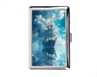 Könnte beinhalten: Ein silbernes Zigarettenetui mit einer detaillierten Illustration eines Großseglers, der auf ruhigem Wasser segelt und sich im Wasser darunter spiegelt. Der Himmel ist mit flauschigen weißen Wolken vor blauem Hintergrund gefüllt.
