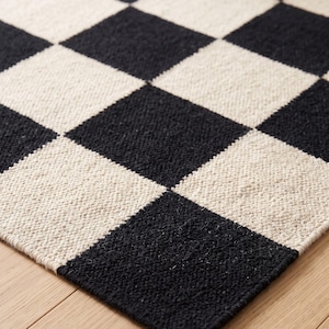 Puede incluir: Una alfombra tejida que presenta un patrón de tablero de ajedrez de alto contraste con cuadrados negros y blanco hueso alternados. La superficie textil muestra una construcción de pelo rizado texturizado y consistente en todo el diseño.