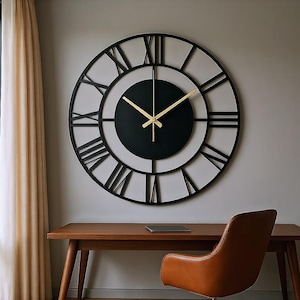 Puede incluir: Un gran reloj de pared redondo con una esfera negra y números romanos. El reloj tiene manecillas doradas y un marco negro. Está montado en una pared gris sobre un escritorio de madera y una silla de cuero marrón.