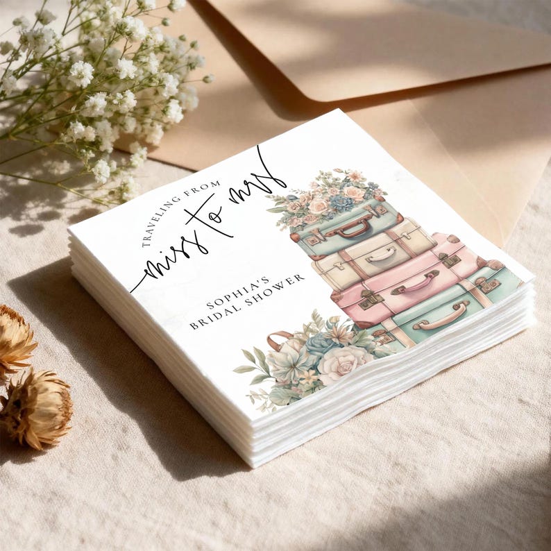 May include: A stack of white paper napkins with a watercolor design for a bridal shower. The design features a stack of vintage suitcases in pastel colors, topped with flowers. Text reads "Traveling from Miss to Mrs" and "Sophia's Bridal Shower."