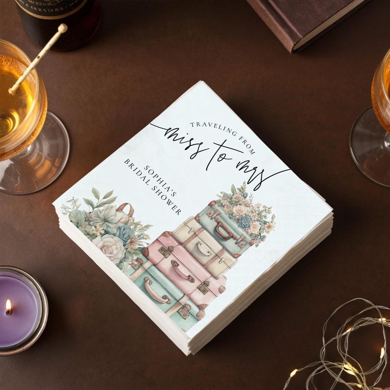 May include: Square white paper napkins with the text "Traveling from Miss to Mrs" and "Sophia's Bridal Shower". The napkins feature a watercolor design of stacked vintage suitcases in pastel colors and floral arrangements.