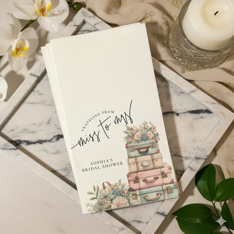 May include: A stack of white bridal shower invitations with the text "Traveling from Miss to Mrs" and "Sophia's Bridal Shower". The invitations feature a watercolor design of stacked vintage suitcases and floral arrangements in pastel colors.