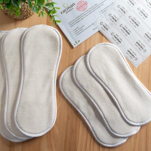 May include: A collection of off-white, oval-shaped absorbent pads with a light gray border, arranged on a wooden surface. The pads are accompanied by a sheet of stickers and a small card with the text "racman stickers".