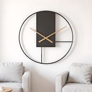 May include: A modern wall clock with a black circular frame and a rectangular black center. The clock hands are made of light-colored wood. The clock is mounted on a white wall, with two gray sofas visible below.