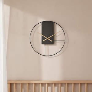 May include: A modern wall clock with a black metal frame and a rectangular black center. The clock hands are gold-colored, and the design includes a partial circle and straight lines. The clock is mounted on a beige wall.
