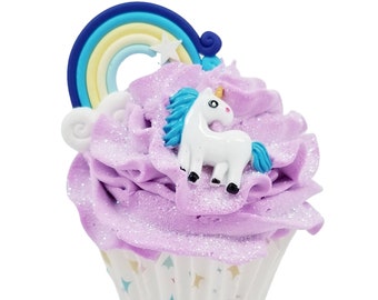May include: A decorative cupcake featuring purple glittery frosting, a white unicorn figurine with a blue mane, and a colorful rainbow arch with a small white star. The cupcake is held in a white paper liner decorated with small, multicolored star shapes.