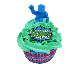 May include: A decorated cupcake with green frosting, a blue superhero figurine, and a "POW!" graphic. The cupcake sits in a red, white, and blue striped liner, perfect for a superhero-themed party or celebration.