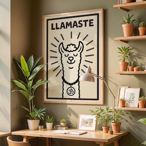Op de afbeelding: Een ingelijste poster met het woord "LLAMASTE" bovenaan. De poster toont een zwart-wit illustratie van een lama met stralende lijnen en een ketting met het Om-symbool. De poster hangt aan een groene muur boven een houten bureau.