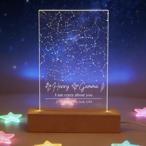 May include: A personalized night light featuring a constellation map with the names "Henry" and "Gemma" and the text "I am crazy about you". The light sits on a wooden base and is surrounded by colorful star-shaped lights.
