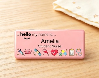 May include: A rectangular pink name badge featuring the text #hello my name is... Amelia Student Nurse. The design includes colorful medical-themed icons such as a syringe, nurse cap, bandage, IV bag, heart with an EKG line, pills, clipboard, and stethoscope.