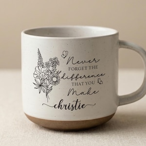 May include: A speckled white ceramic mug with a brown base and a curved handle. The mug features a floral illustration and the text "Never forget the difference that you make Christie."