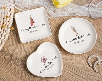 May include: Three white ceramic ring dishes in square, round, and heart shapes. Each dish has a gold rim, a floral design, a name, and a date. The square dish says "janice" and the date "02.16.2025".