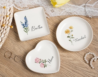 May include: Three white ceramic trinket dishes in square, round, and heart shapes. Each dish has a gold rim and a floral design with a name. The square dish has blue flowers and the name "Bertha". The round dish has yellow flowers and the name "Rachel". The heart dish has pink flowers and the name "Elma".