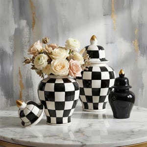 Puede incluir: Un conjunto de jarrones decorativos con un diseño a cuadros en blanco y negro. Un jarrón contiene un ramo de rosas. Las tapas de los jarrones tienen detalles dorados. Los jarrones se exhiben sobre una superficie de mármol.