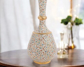 Può includere: Un vaso decorativo con base bianca, ornato da un motivo floreale dettagliato in rosso, blu e giallo. Il vaso presenta accenti dorati attorno alla base, al collo e a una fascia centrale. Il vaso è alto circa 30 cm.