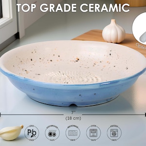 May include: A ceramic garlic grater bowl with a blue rim and a white interior speckled with brown. The bowl is 18 cm in diameter and 4 cm high. The text "TOP GRADE CERAMIC" is at the top.