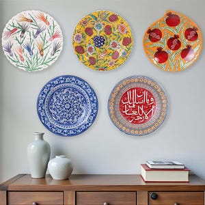 Può includere: Una collezione di piatti decorativi con motivi floreali e di melograno. I piatti sono montati su una parete sopra un mobile in legno. I piatti presentano vari colori, tra cui blu, giallo, rosso e arancione.