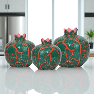 May include: Three ceramic pomegranate sculptures in varying sizes. The green bodies are adorned with red vein-like patterns and topped with pink crowns. The surfaces have a speckled, glittery finish, adding a touch of sparkle to the decorative pieces.