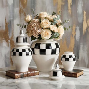 Op de afbeelding: Een verzameling decoratieve keramische vazen met een zwart-wit geblokt patroon. De witte vazen hebben zilveren accenten en zijn gerangschikt met een boeket rozen en hortensia's. De vazen staan op een marmeren oppervlak.