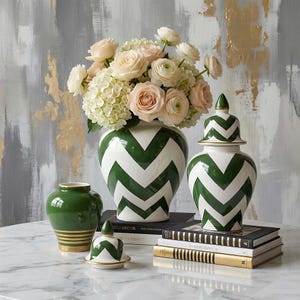 Könnte beinhalten: Dekorative Keramikvasen und -gläser. Die Vasen haben einen weißen Hintergrund mit einem kräftigen grünen Zickzackmuster. Eine Vase enthält einen Strauß aus rosa Rosen und weißen Hortensien. Ein kleiner grüner Vase und ein Glas mit Deckel sind ebenfalls vorhanden.
