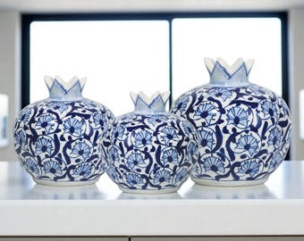 May include: Three ceramic pomegranate-shaped vases with a blue and white floral pattern. The vases vary in size and have a crown-like top. The vases are displayed on a white surface.