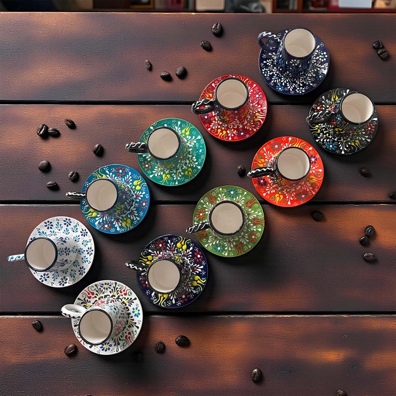 May include: A collection of colorful, patterned ceramic coffee cups and saucers. The cups and saucers feature intricate floral designs in various colors, including blue, red, green, and white. The arrangement is on a dark wooden surface with scattered coffee beans.