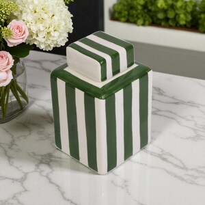 Pu&ograve; includere: Un vaso quadrato in ceramica con coperchio, caratterizzato da strisce verticali verdi e bianche. Il vaso &egrave; un oggetto decorativo, possibilmente per la conservazione o l'esposizione. Il coperchio ha lo stesso motivo a strisce.