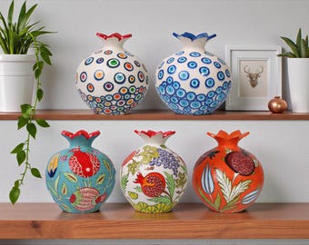 May include: Six decorative ceramic vases with pomegranate shapes. The vases are hand-painted with colorful patterns and designs, including floral and geometric motifs. The vases are displayed on a wooden shelf.