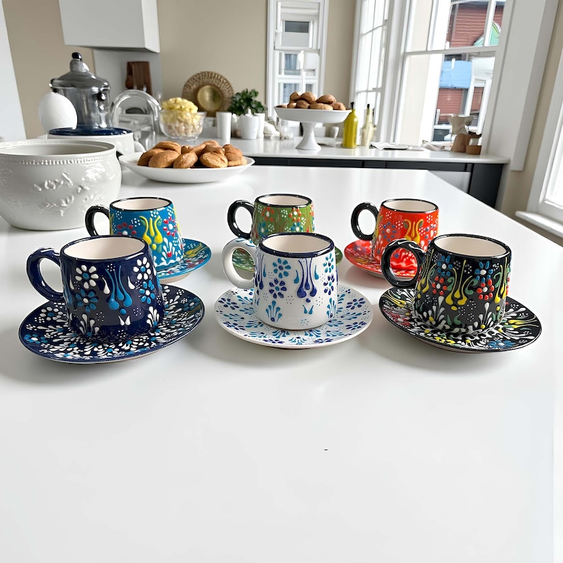 May include: A collection of six small, decorative coffee cups and saucers. The cups feature colorful floral patterns in blue, red, green, and black. Each cup sits on a matching saucer, creating a vibrant and artistic display.