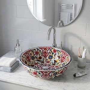 May include: A decorative, round ceramic bathroom sink with a vibrant floral pattern in red, blue, yellow, and white. The sink has a dark blue rim and is set on a marble countertop. A chrome faucet is installed above the sink.