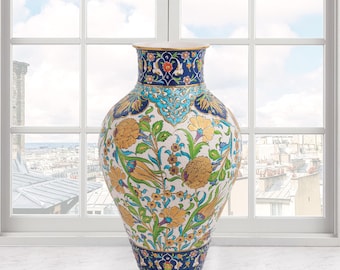 Può includere: Un grande vaso di ceramica ornato. Il vaso ha un corpo largo e un collo stretto. Presenta uno sfondo bianco con intricati motivi floreali in oro, blu, turchese e verde. I bordi superiore e inferiore sono blu scuro con disegni floreali.