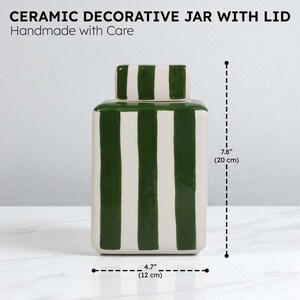Pu&ograve; includere: Vaso decorativo in ceramica con coperchio, fatto a mano. Il vaso bianco presenta strisce verticali verdi e un coperchio abbinato. Misura 12 cm di larghezza e 20 cm di altezza.