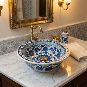 Puede incluir: Un lavabo de cerámica redondo con base blanca y complejos patrones florales en azul y azul claro. El lavabo incluye un tapón de drenaje central de latón y está colocado sobre una encimera de mármol blanco con un dispensador de jabón.