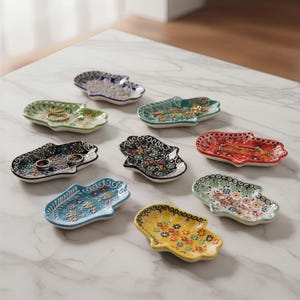 May include: A collection of eight hand-shaped ceramic trinket dishes in various colors, including blue, green, red, and yellow. Each dish features a floral pattern and is designed to hold small jewelry items.