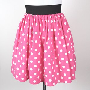 May include: A pink skirt with white polka dots and a black waistband.