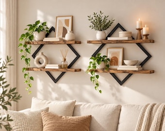 May include: Two wall-mounted shelving units featuring black metal diamond-shaped frames and two horizontal wooden shelves each. The shelves hold potted green plants, framed abstract art, white ceramic vases, books, a reed diffuser, and candles.