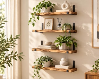 May include: Four horizontal wooden shelves with natural grain patterns mounted on a wall using black metal brackets. The shelves hold various decorative items including potted green plants, white ceramic vases, books, and a framed botanical print.