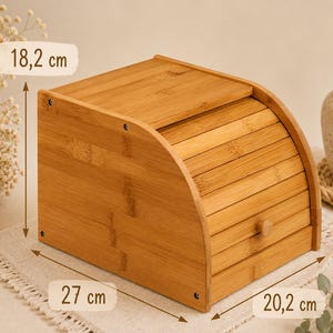 May include: A light brown bamboo bread box with a roll-top door and a small wooden knob. The box features visible dimensions of 18.2 cm in height, 27 cm in depth, and 20.2 cm in width, constructed with horizontal slats and side panels.