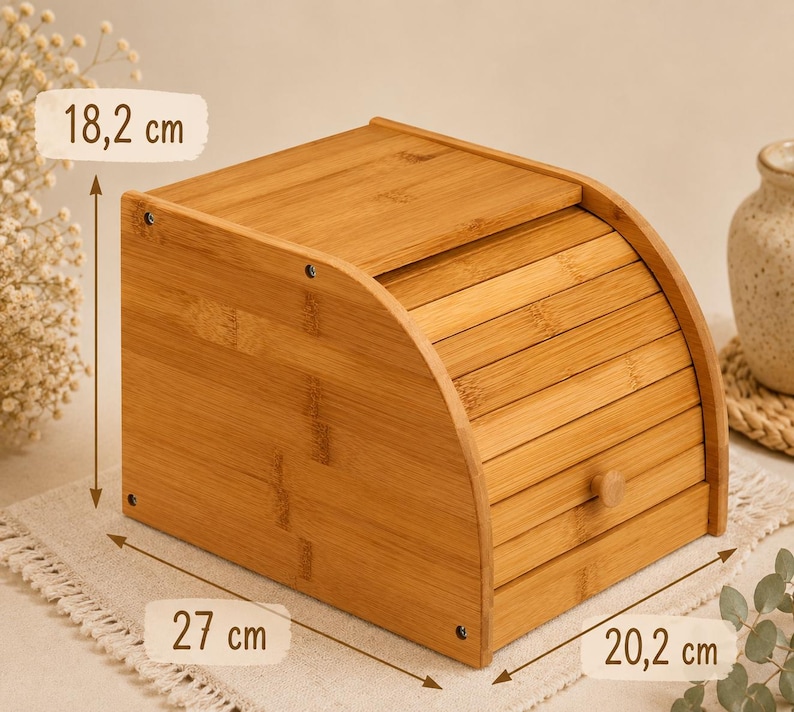 May include: A light brown bamboo bread box with a roll-top door and a small wooden knob. The box features visible dimensions of 18.2 cm in height, 27 cm in depth, and 20.2 cm in width, constructed with horizontal slats and side panels.