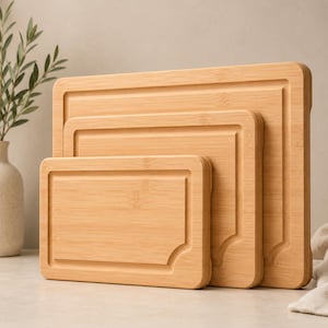 May include: A set of three rectangular bamboo cutting boards of varying sizes, each featuring a light tan wood grain, rounded corners, and a recessed juice groove running along the inner perimeter of the front face of each board.