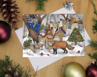 May include: A Christmas card depicting a winter woodland scene with a fox, two deer, a raccoon, a rabbit, and a small mouse. The animals are gathered around a small Christmas tree adorned with red baubles. The card has a white background with a silver glitter effect.