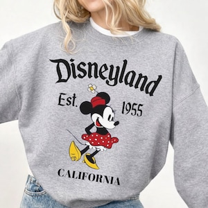 May include: A grey sweatshirt with the Disneyland logo, the text "Est. 1955" and "California." The graphic features a cartoon Minnie Mouse in a red polka dot dress and yellow shoes.