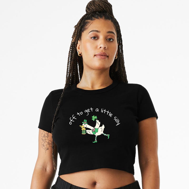 May include: Black crop top with the phrase "off to get a little silly" in cursive. The graphic features a cartoon goose wearing a leprechaun hat and striped socks, holding a beer and a shamrock. The shirt is a crew neck.
