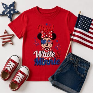 K&ouml;nnte beinhalten: Rotes T-Shirt mit einem Minnie Mouse-Motiv, das herzf&ouml;rmige Sonnenbrillen mit Sternen- und Streifen-Design tr&auml;gt. Auf dem Shirt steht "Red White & Minnie". Enth&auml;lt rote Turnschuhe, Jeansshorts und eine kleine amerikanische Flagge.