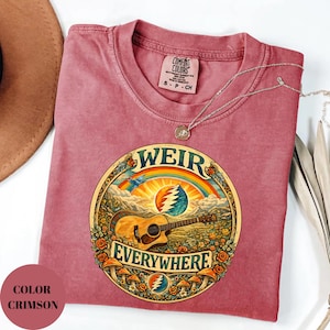 May include: Crimson-coloured t-shirt with a round graphic featuring a guitar, rainbow, and the words "WEIR EVERYWHERE." The design includes a mountain landscape, flowers, and mushrooms. The shirt has a crew neck and short sleeves.