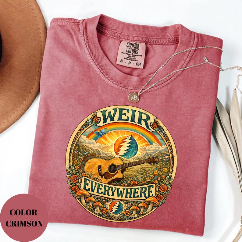May include: Crimson-coloured t-shirt with a round graphic featuring a guitar, rainbow, and the words "WEIR EVERYWHERE." The design includes a mountain landscape, flowers, and mushrooms. The shirt has a crew neck and short sleeves.