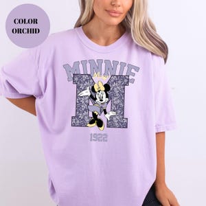 Pu&ograve; includere: T-shirt color orchidea con grafica di Minnie Mouse. Il design include la scritta "MINNIE" sopra una "M" a fantasia floreale e l'anno "1922". La maglietta ha maniche corte e una vestibilit&agrave; rilassata.