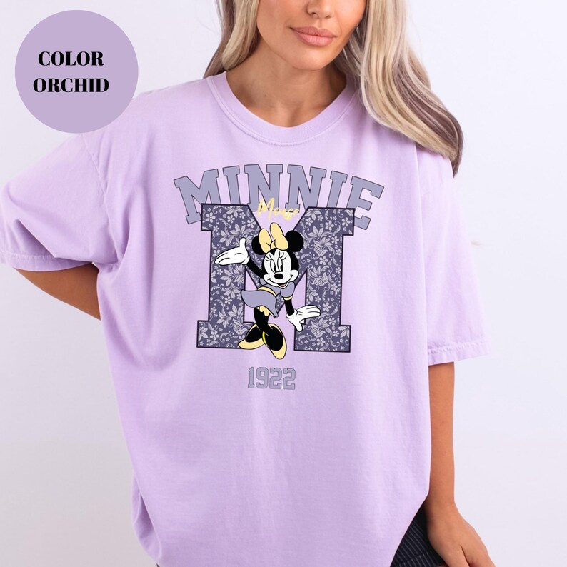 Pu&ograve; includere: T-shirt color orchidea con grafica di Minnie Mouse. Il design include la scritta "MINNIE" sopra una "M" a fantasia floreale e l'anno "1922". La maglietta ha maniche corte e una vestibilit&agrave; rilassata.