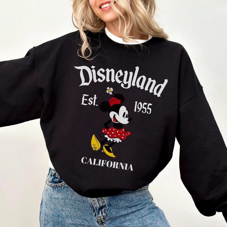 May include: Black sweatshirt featuring the Disneyland logo, Minnie Mouse graphic, and the text "CALIFORNIA". The sweatshirt has a white collar and long sleeves. The Disneyland logo is in white, with the year "1955" below the logo.